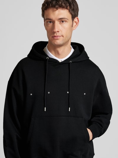 Männermodel trägt Relaxed Fit Hoodie aus reiner Baumwolle Modell 'DOLAND' von HUGO, schwarz, unifarben, Nahaufnahme Oberkörper.