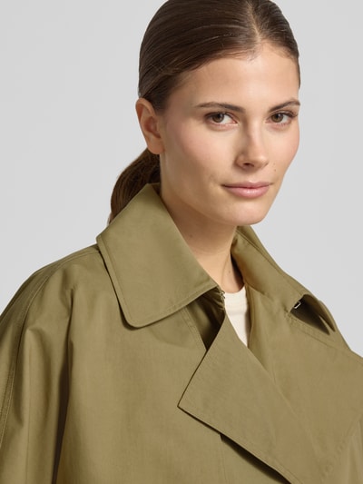 Vrouwenmodel draagt Trenchcoat met verdekte sluiting en strikceintuur van Blonde No. 8 in katoenmix, getailleerd model, platte kraag, nahaufnahme bovenlichaam.