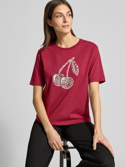Frauenmodel trägt T-Shirt mit Motiv-Print von Marc Cain in Dunkelrot, reine Baumwolle, Regular Fit, Nahaufnahme Oberkörper.