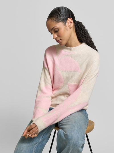 Frauenmodel trägt Oversized Strickpullover mit gerippten Abschlüssen Modell 'OMEA' von B.Young, Material-Mix mit Woll-Anteil, Rundhalsausschnitt, creme mit rosa Muster, lockere Form, Jeans, Nahaufnahme Oberkörper.