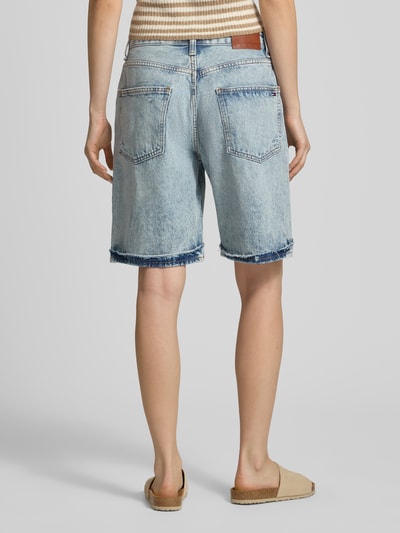 Kobiece model prezentuje szorty jeansowe Relaxed Fit Jeansshorts aus Baumwoll-Lyocell-Mix od Tommy Jeans, efekt znoszenia, wyhaftowane logo, naszywka z logo, 5 kieszeni, zapięcie na guzik i zamek błyskawiczny, szlufki na pasek, wykończenie nogawek z frędzlami, mieszanka bawełny i lyocellu, całkowity widok z tyłu
