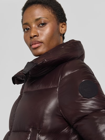 Frauenmodel trägt Regular Fit Steppjacke mit Stehkragen Modell 'Isla' von Save The Duck, dunkles Braun, glänzende Stepp-Optik, Nahaufnahme Oberkörper.