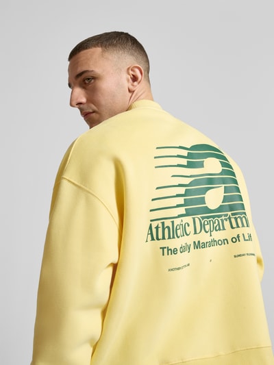 Männermodel trägt Sweatshirt mit Statement-Prints Modell 'Athletic Department' von ANOTHER COTTON LAB in Gelb mit grüner Aufschrift, Baumwoll-Mix, Loose Fit, gerippter Stehkragen, überschnittene Schultern, Rückenansicht, Nahaufnahme Oberkörper.