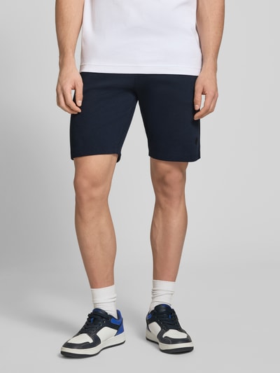 Männermodel trägt Straight Fit Shorts mit Logo-Stitching Modell 'Fillip' von Blend aus Reine Baumwolle mit Strukturmuster, Eingrifftaschen, Gesäßtaschen und elastischem Bund mit Tunnelzug, Bundweite bei Größe M 39 cm, Innenbeinlänge 26 cm, Ganzkörperansicht von vorne.