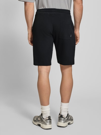 Mężczyznamodel nosi Straight Fit Shorts mit Logo-Stitching Modell 'Fillip' od Blend, czarne, bawełna, elastyczny pas, kieszenie, strukturalna faktura, szerokość w rozmiarze M: 39 cm, długość nogawki wewnętrznej: 26 cm, widok całej sylwetki z tyłu.