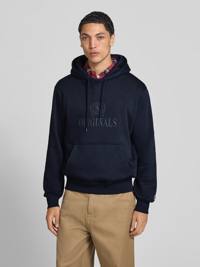 Männermodel trägt Hoodie aus Baumwoll-Mix Modell 'FREDERIKS' von JACK & JONES in Dunkelblau, Kängurutasche, Label-Print, Ganzkörperansicht von vorne.