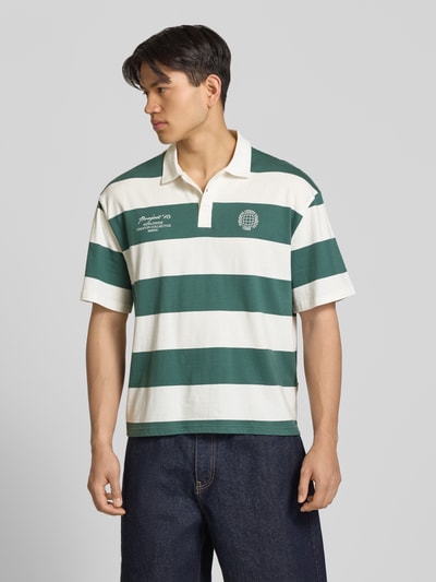 Męski model nosi Relaxed Fit Poloshirt aus reiner Baumwolle Modell 'DEVIN' von Only & Sons, efekt: wzór w paski, krój relaxed fit, nadruk z motywem, aplikacja z metką, kołnierzyk polo, dekolt w serek, krótkie zapięcie na guziki, krótki rękaw, dżersej, bawełna; kolor zielony i ecru; Ganzkörperansicht z przodu.