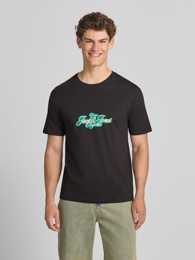 Männermodel trägt Herren T-Shirt mit Label-Print Modell 'CASSIS' von Jack & Jones, Reine Baumwolle, Regular-Fit, Rundhalsausschnitt, schwarze Farbe, mittiger Print, Rückenlänge bei Größe M 68 cm, Ganzkörperansicht von vorne.