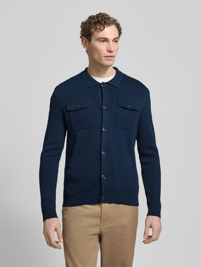 Männermodel trägt Strickjacke mit Knopfleiste Modell 'Owero' von JOOP! Collection in Dunkelblau aus reiner Baumwolle, Regular-Fit, Kentkragen, Brusttaschen mit Knopfverschluss, gerippte Abschlüsse, Label-Detail, Rückenlänge 70 cm, Ärmellänge 73 cm, Ganzkörperansicht von vorne.