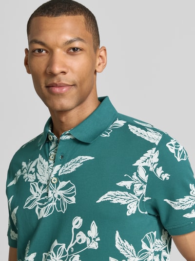 Männermodel trägt Modern Fit Poloshirt mit Label-Detail von Lerros in Grün mit weißem floralen Muster aus reiner Baumwolle, Nahaufnahme Oberkörper.