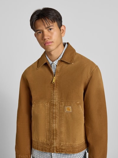 Männermodel trägt Jacke mit Reißverschluss und Label-Detail Modell 'Dearborn' von Carhartt Work In Progress aus brauner Baumwolle, Nahaufnahme Oberkörper. Relaxed Fit, Umlegekragen, Eingrifftaschen, sichtbare Struktur.