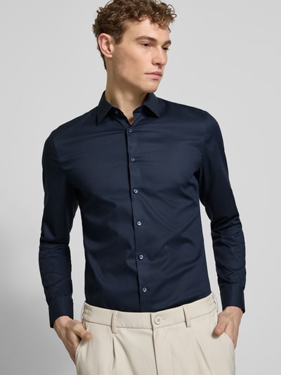 Męski model nosi Slim Fit Businesshemd mit Kentkragen von OLYMP No. Six, granatowy, długi rękaw, bawełna elastyczna, krój slim fit, z przodu, zbliżenie na górną część sylwetki, długość pleców w rozmiarze 40: 81 cm, szerokość ramion w rozmiarze 40: 43 cm, długość rękawa w rozmiarze 40: 67 cm.