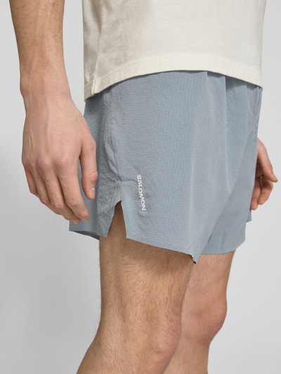 Männermodel trägt Shorts mit elastischem Logo-Bund Modell 'SENSE AERO' von Salomon, hellgrau, Strukturstoff, Nahaufnahme Oberschenkel, Material-Mix mit Stretch-Anteil, Loose Fit, Logo-Print.