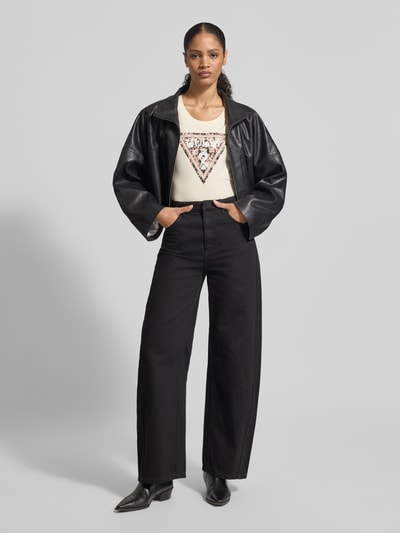 Vrouwenmodel draagt Slim Fit T-shirt met Ziersteinbesatz van Guess in lichte kleur, katoenmix, logodetail, ronde hals, Ganzkörperansicht von voren.