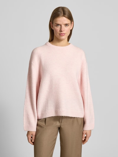 Vrouwenmodel draagt Gebreide pullover met wol van Gina Tricot in lichtroze, materiaalmix, los model, ribboorden, ronde hals, ruglengte 59 cm, mouwlengte 66 cm. Ganzkörperansicht von vorne.