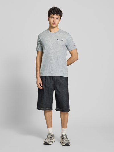 Męski model trägt T-Shirt mit Logo-Stitchings Modell 'ICONS CONTRAST' von CHAMPION, mieszanka bawełny, nowoczesny krój, okrągły dekolt, długość tyłu w rozmiarze M: 70 cm, Ganzkörperansicht von vorne.