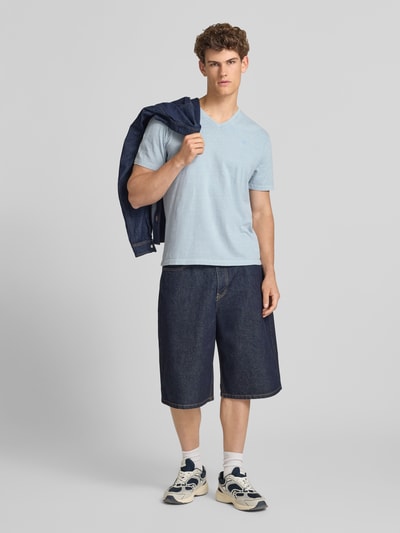Männermodel trägt T-Shirt aus Baumwoll-Leinen-Mix mit V-Ausschnitt von Superdry in Hellblau, kombiniert mit weiter Jeansshorts, Ganzkörperansicht von vorne. Regular Fit, sichtbares Stitching, Rückenlänge bei Größe M: 68 cm.