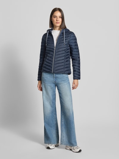 Frauenmodel trägt Regular Fit Steppjacke mit Kapuzenkragen von Tom Tailor in Dunkelblau, kombiniert mit Jeans, Ganzkörperansicht von vorne, Damen Steppjacke von Tom Tailor.