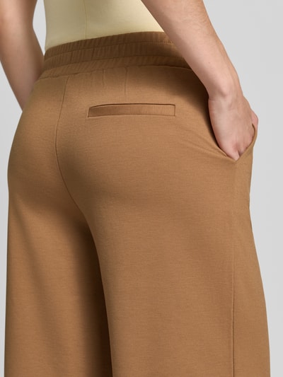 Frauenmodel trägt Wide Fit Hose mit Viskose-Anteil Modell 'Kate' von ICHI in Braun, sichtbare Bundfalten und Eingrifftasche, Nahaufnahme Rückansicht.