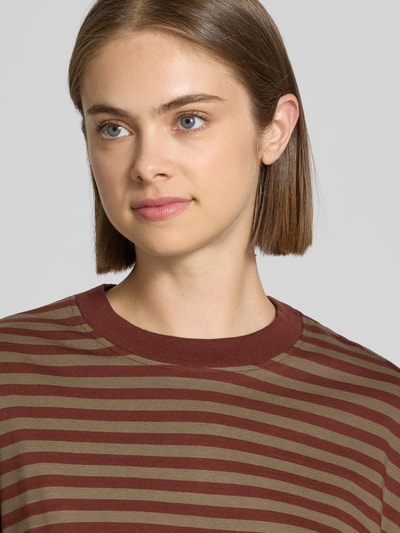 Modelka kobieca nosi Relaxed Fit Langarmshirt aus reiner Baumwolle od Gina Tricot, paski brązowo-oliwkowe, okrągły dekolt, bawełna, bluzka z długim rękawem, długość tyłu w rozmiarze S: 62 cm, zbliżenie na górną część ciała