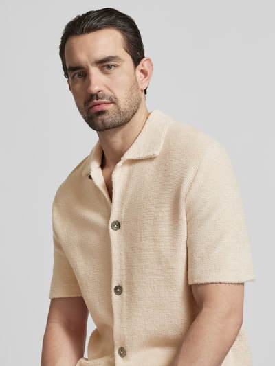Męski model nosi Hemdjacke mit Kaschmir-Anteil von FTC Cashmere, mieszanka bawełny i kaszmiru, krój regular fit, kołnierzyk polo, listwa guzikowa, rękaw o dł. 1/2, kremowy odcień, tekstura miękka, widoczna struktura tkaniny, półzbliżenie na górną część ciała.