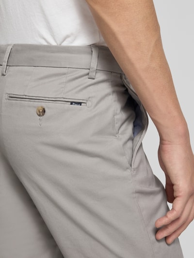 Mężczyzna nosi Slim Fit Chino aus Baumwoll-Mix von Polo Ralph Lauren, efekt: jednolity kolor, krój slim fit, detal z logo, 5 kieszeni, mieszanka bawełny, detal: zapięcie na guzik i zamek błyskawiczny, szlufki na pasek, zdjęcie: zbliżenie na tylną kieszeń z boku.