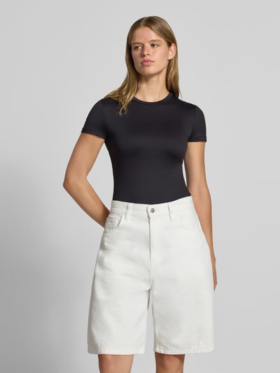 Frauenmodel trägt schwarzes Slim Fit T-Shirt mit Rundhals Modell 'LULA' von PIECES, kombiniert mit weißer Shorts, Nahaufnahme Oberkörper.