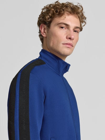 Männermodel trägt Regular Fit Sweatjacke aus Baumwoll-Mix Modell 'Felpa' von Armani Exchange in Blau mit schwarzen Details, Nahaufnahme Oberkörper, Kontext: elastischer Baumwoll-Mix, Stehkragen, Zweiwege-Reißverschluss, Eingrifftaschen, elastische Abschlüsse.