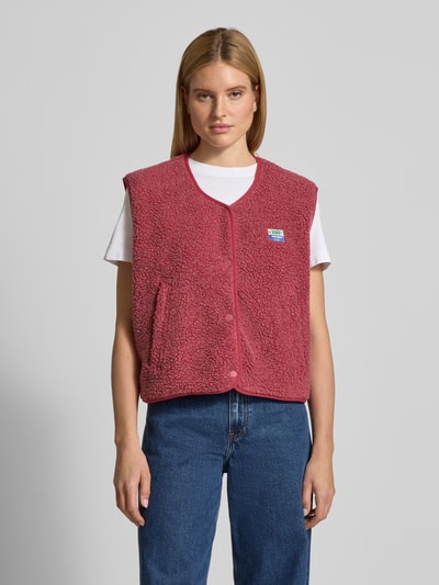 Frauenmodel trägt Weste mit Rundhalsausschnitt Modell 'HOKTOWN' von American Vintage aus rotem Teddyfell, aufgesetzte Taschen, Ganzkörperansicht von vorne.