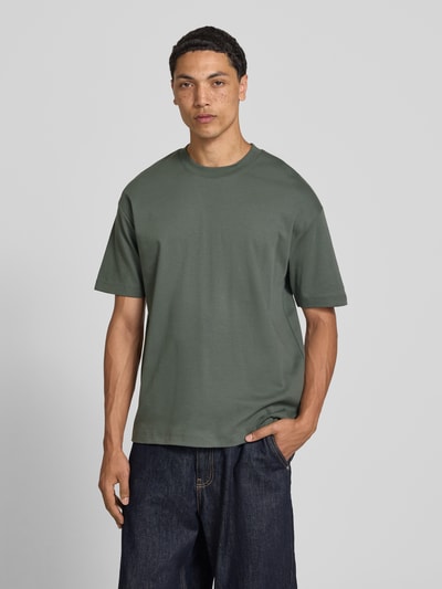 Männermodel trägt Relaxed Fit T-Shirt aus reiner Baumwolle von Marc O'Polo Denim in dunklem Grün, glatte Textur, Herren T-Shirt, Ganzkörperansicht von vorne.