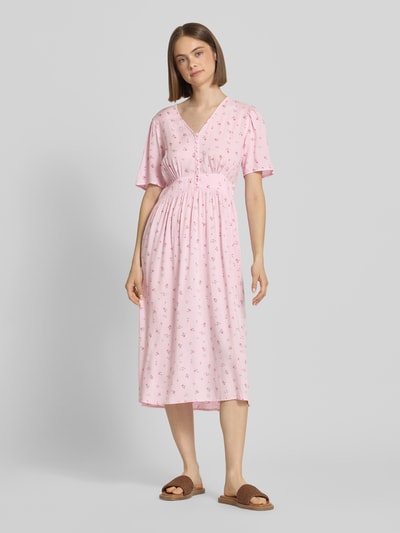 Frauenmodel trägt A-Linien Midikleid aus reiner Viskose Modell 'TALA' von Pieces, rosa mit Allover-Muster, kurze Knopfleiste, Ganzkörperansicht von vorne.