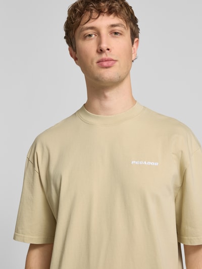 Männermodel trägt Oversized T-Shirt mit Logo-Stitching von Pegador aus Reine Baumwolle, Oversized-Fit, Rundhalsausschnitt, Nahaufnahme Oberkörper. Rückenlänge bei Größe M: 73 cm.