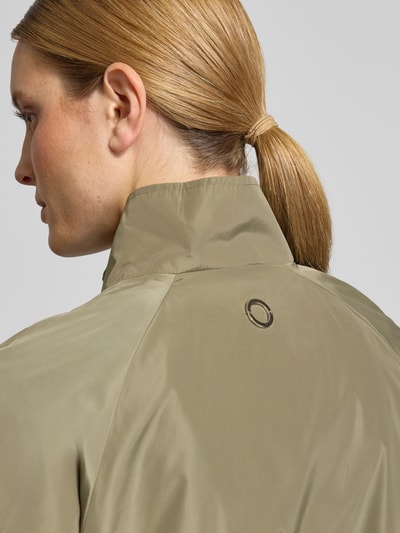 Frauenmodel trägt Jacke mit elastischen Abschlüssen und stójka von Fuchs Schmitt, prosty krój, raglanowe rękawy, zamek błyskawiczny, długość tyłu w rozmiarze 36: 56 cm, szerokość ramion w rozmiarze 36: 38 cm, szerokość klatki piersiowej w rozmiarze 36: 48 cm, długość rękawów w rozmiarze 36: 43 cm, jednolita oliwkowa kolorystyka, gładka tekstura, detalaufnahme Rückansicht.