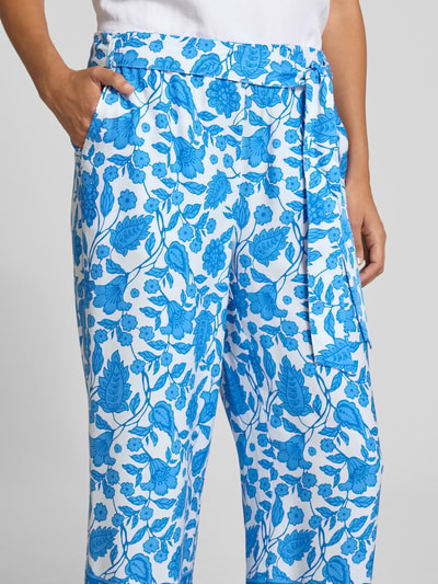 Frauenmodel trägt Straight Fit Stoffhose aus Reiner Viskose von More & More mit Floraler-Print Allover-Print, Zierschleife, Nahaufnahme Oberkörper. Passform Verkürzt, elastischer Bund, Bundweite 37 cm, Innenbeinlänge 64 cm, weiße Grundfarbe mit blauem Florales-Allover-Muster.