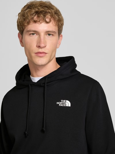 Männermodel trägt Regular fit hoodie mit capuchon Model "EVOLUTION BOX" van The North Face in zwart katoenmix, Nahaufnahme Oberkörper. Context: Heren hoodie van The North Face, katoenmix, regular fit, model "EVOLUTION BOX", capuchon met tunnelkoord, kangoeroezak, elastische boordjes, ruglengte bij maat M: 67 cm, mouwlengte bij maat M: 68 cm.
