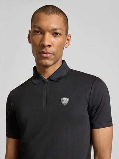 Männermodel trägt Slim Fit Poloshirt aus Viskose-Mix von EA7 Emporio Armani in Schwarz mit Logo-Detail, Nahaufnahme Oberkörper.