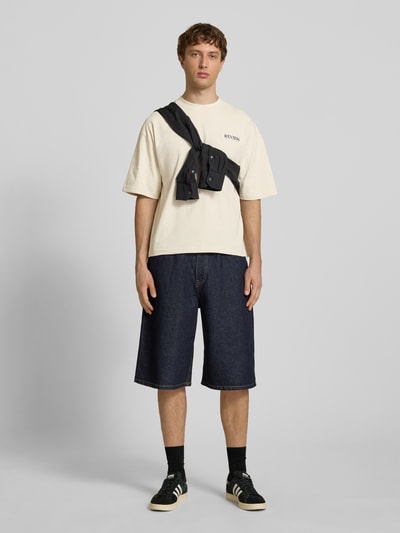 Männermodel trägt T-Shirt mit Label-Detail von REVIEW in Creme, Reine Baumwolle, Lockerer-Schnitt, Rundhalsausschnitt, 1/2-Arm, Rückenlänge bei Größe M 66 cm, Ganzkörperansicht von vorne.