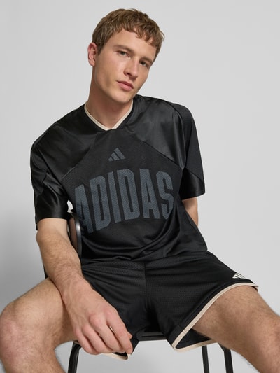 Männermodel trägt T-Shirt mit V-Ausschnitt und Logo-Print von adidas Sportswear in Schwarz, lockerer Schnitt, Nahaufnahme Oberkörper.