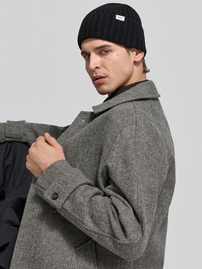 Mannenmodel draagt Beanie aus Woll-Mix van Forét in zwart met ribstructuur, brede omslag, labelpatch en logo, detailopname zijaanzicht