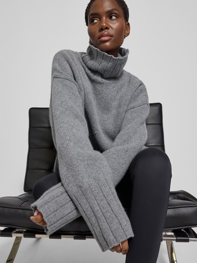 Frauenmodel trägt Oversized Pullover aus reiner Wolle von black palms in Grau mit gerippten Abschlüssen, Rollkragen, Rückenlänge 56 cm, Nahaufnahme Oberkörper.