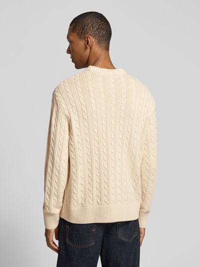 Männermodel trägt Relaxed Fit Pullover aus reiner Baumwolle Modell 'BRAUN' von Selected in Zopfmuster-Strickoptik, cremefarben, Ganzkörperansicht Rückansicht.