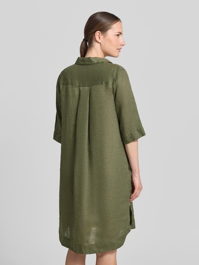Frauenmodel trägt knielanges Leinenkleid Modell 'DERRY' von 0039 Italy in Olivgrün, Gerader-Schnitt, Hemdblusenkragen, Rückenlänge 99 cm, Brustweite 53 cm, Ärmellänge 37 cm, Reines Leinen, Ganzkörperansicht Rückansicht.