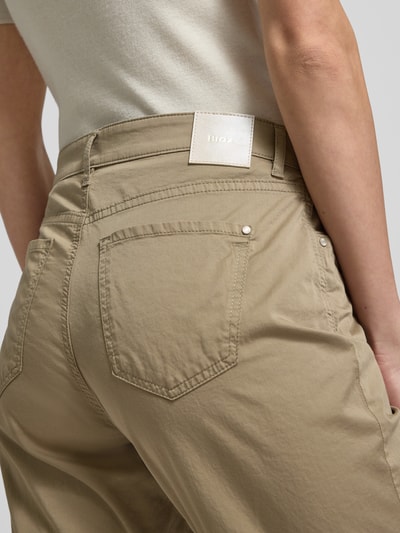 Kobiece model prezentuje spodnie z wpuszczanymi kieszeniami model 'Carola' od Brax, mieszanka bawełny i lyocellu, krój regular fit, szerokość w rozmiarze 36K: 39 cm, długość wewnętrzna nogawki: 76 cm, ujęcie z tyłu na wysokości pasa.