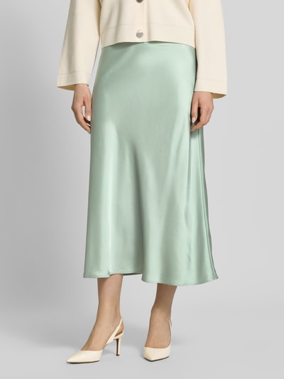 Frauenmodel trägt Midirock in schimmerndem Design von comma, mintgrün, glatte Textur, gerader Schnitt, Nahaufnahme Unterkörper. Material-Mix mit Viskose-Anteil.
