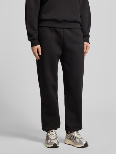 Frauenmodel trägt Basic Sweatpant mit Bündchen am Saum und seitlichen Taschen von Review in Schwarz, lockere Passform, Nahaufnahme Unterkörper.