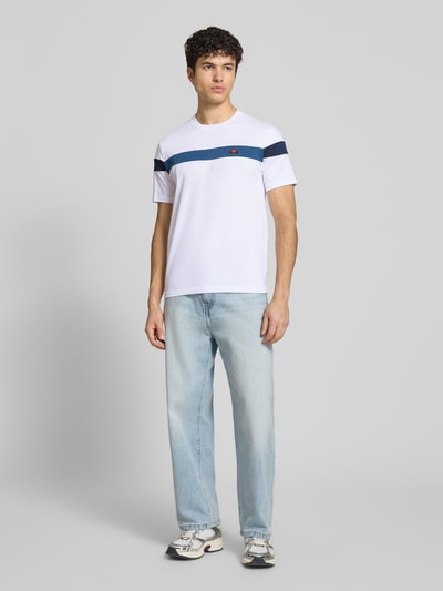 Männermodel trägt Regular Fit T-Shirt mit Logo-Detail Modell 'Caserio' von Ellesse aus reiner Baumwolle, weiß mit blauer Zierlinie, Rundhalsausschnitt, Kurzärmelig, Rückenlänge bei Größe M 68 cm, Ganzkörperansicht von vorne.