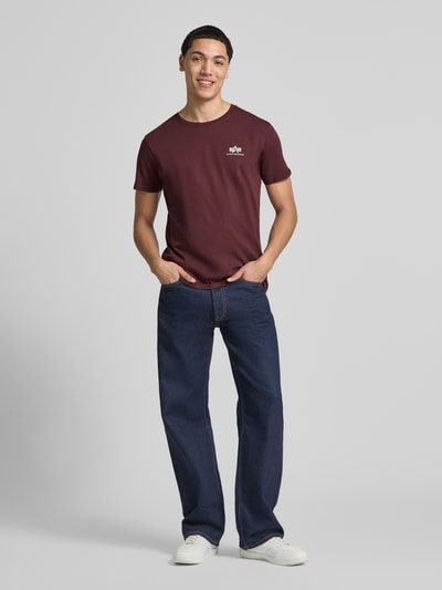 Männermodel trägt T-shirt mit Label-Details Modell 'BASIC' von Alpha Industries in bordeaux, puur katoen, recht model, ronde hals, ruglengte maat M 67 cm, vooraanzicht volledige lichaamsopname.
