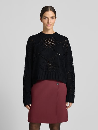 Modelka kobieca nosi Relaxed Fit Strickpullover mit Woll-Anteil od Liu Jo White, czarny sweter z mieszanki wełny, ażurowy wzór, długie rękawy, prążkowane wykończenia i dekolt, długość tyłu w rozm. S: 52 cm, długość rękawa: 51 cm, widok całej sylwetki z przodu.