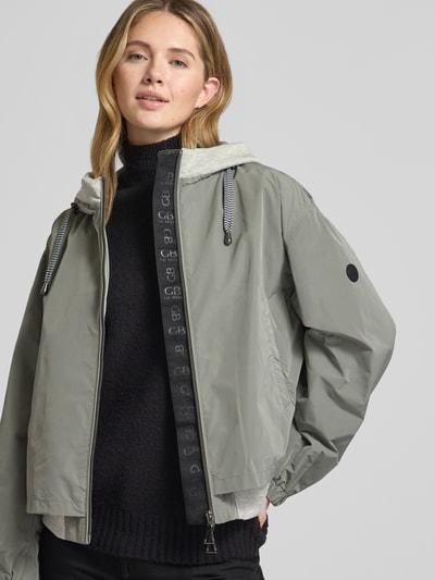 Frauenmodel trägt Jacke mit Zweiwege-Reißverschluss von Gil Bret in Grau mit Kapuze und Eingrifftaschen, Relaxed Fit, Nahaufnahme Oberkörper. Rückenlänge 59 cm, Schulterbreite 52 cm, Brustweite 57 cm, Ärmellänge 57 cm bei Größe 36.