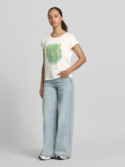 Frauenmodel trägt Regular Fit T-Shirt aus Viskose-Mix mit Statement-Print von Christian Berg Woman, helle Farben, Rundhalsausschnitt, lockere Passform, kombiniert mit weiter Jeans, Ganzkörperansicht von vorne.
